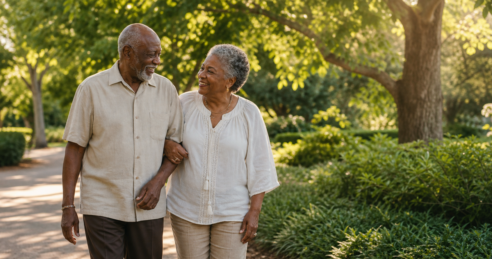 An older Black couple walking arm in arm through a sunny green park